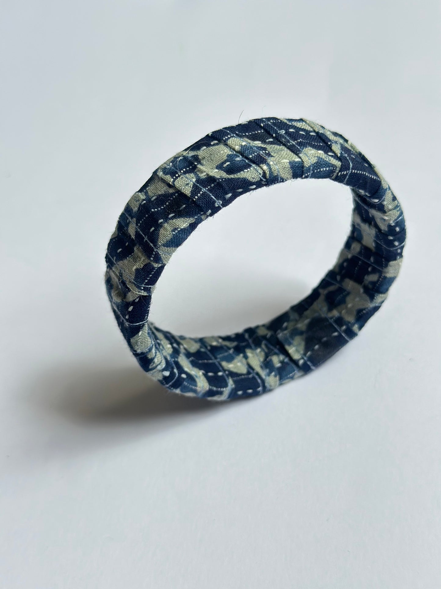 Blue and white patterned handmade fabric bangle bracelet on a light gray background