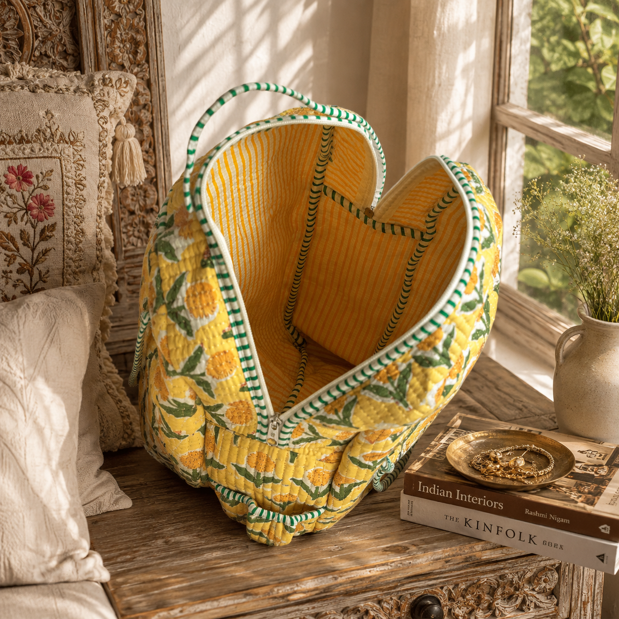 A yellow quilted fabric backpack with a orange and green floral pattern, featuring green and white striped trim, styled on a rustic wooden table next to a window.