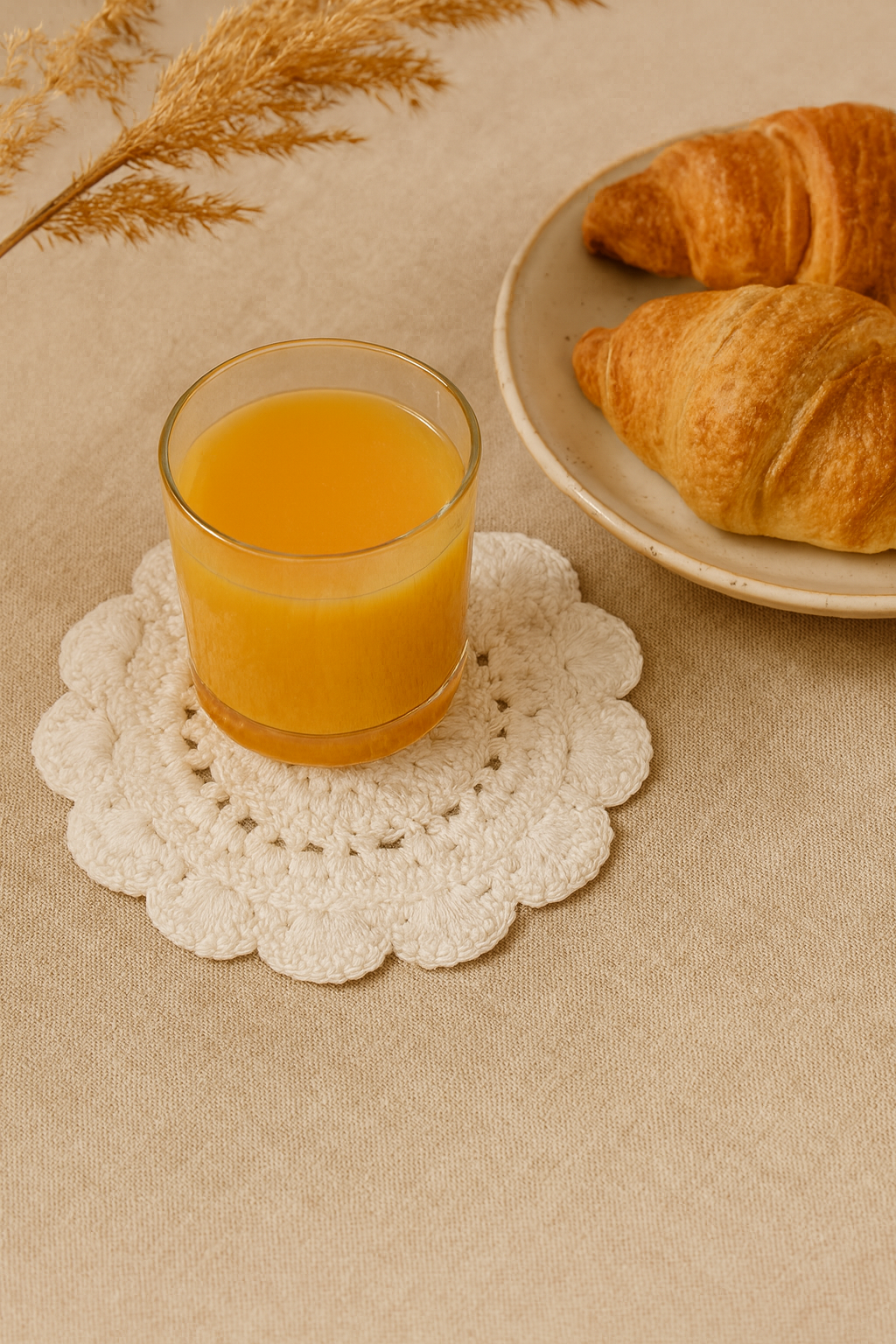 Glass of orange juice on a white crocheted coaster with croissants on a plate in the background