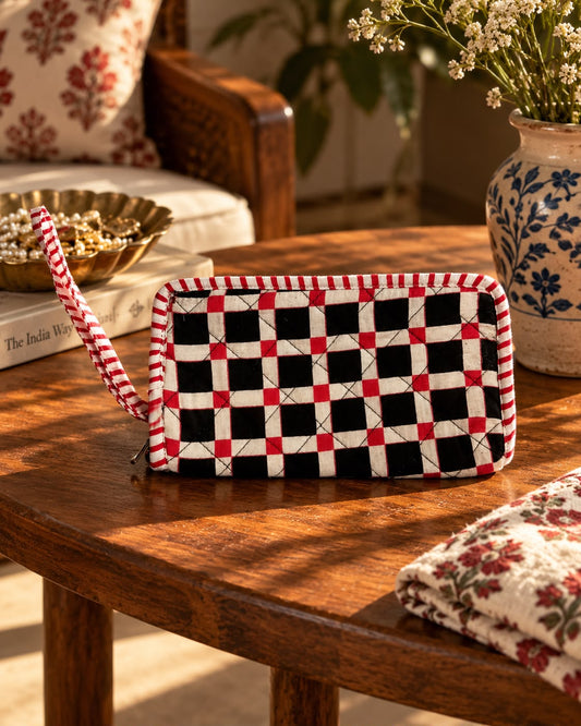 Black & white with a red checkered wallet clutch on a wooden table with a vase with flowers. 