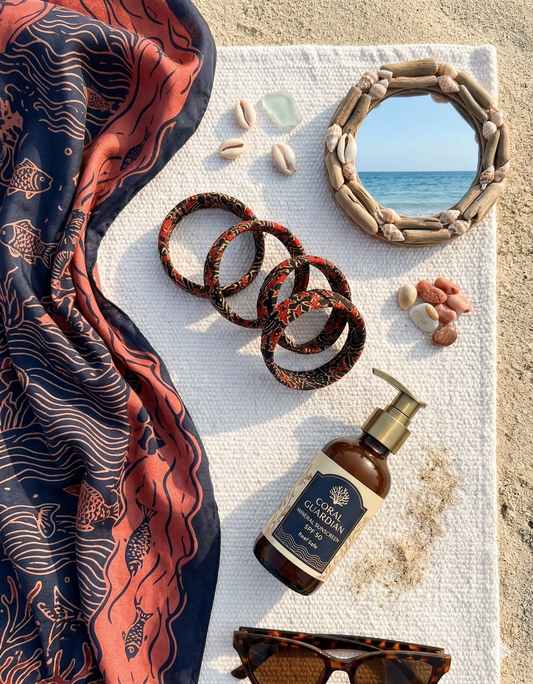 Scarf, fabric bracelets in red & black, bottle, and sunglasses on a towel with a beach view.