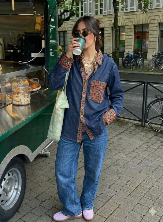 Woman in a blue denim with red cotton patchwork Shirt and jeans drinking from a coffee cup on a city street.