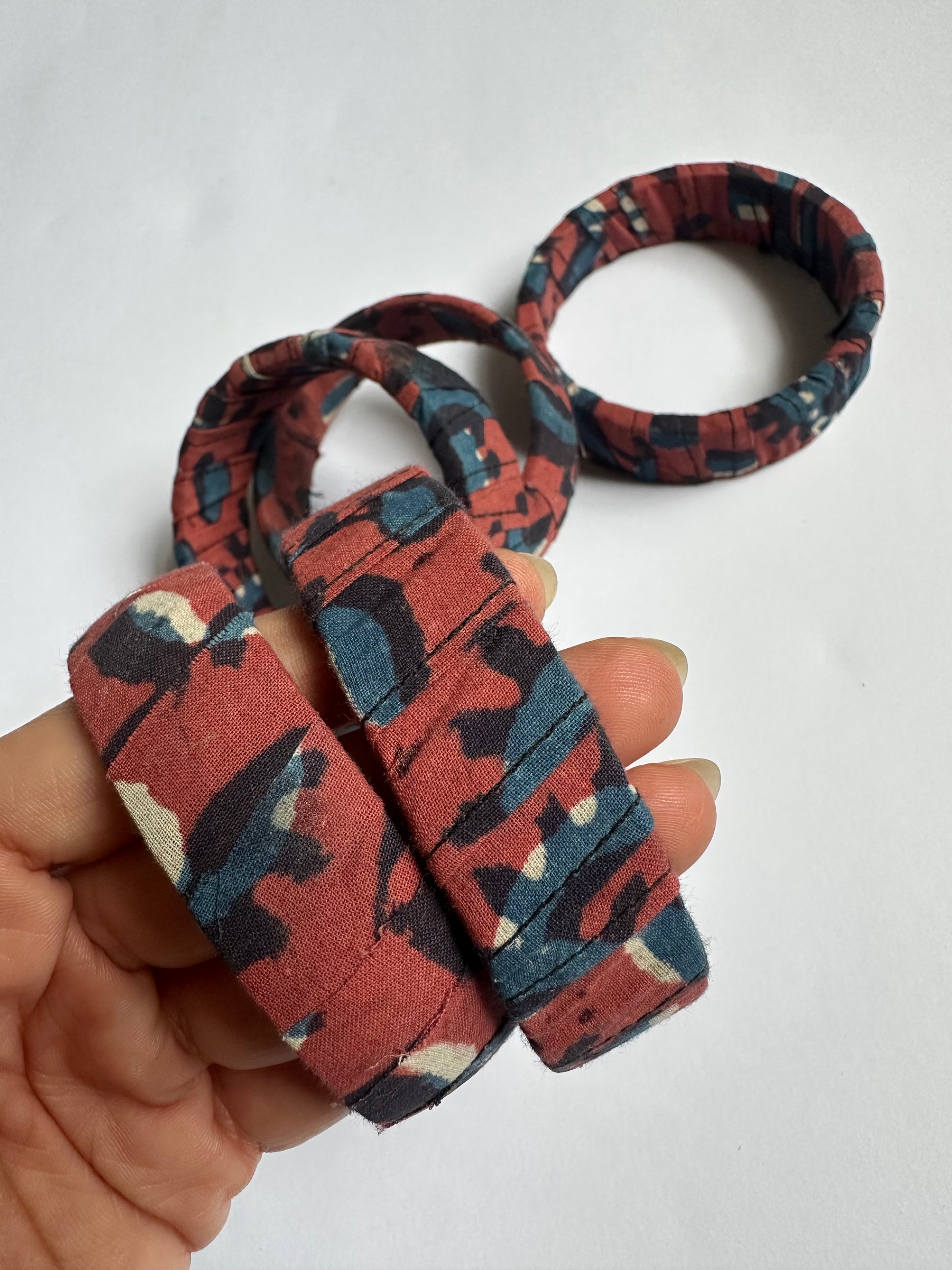 Patterned red & blue fbric handmade bangle  held by a hand on a light background