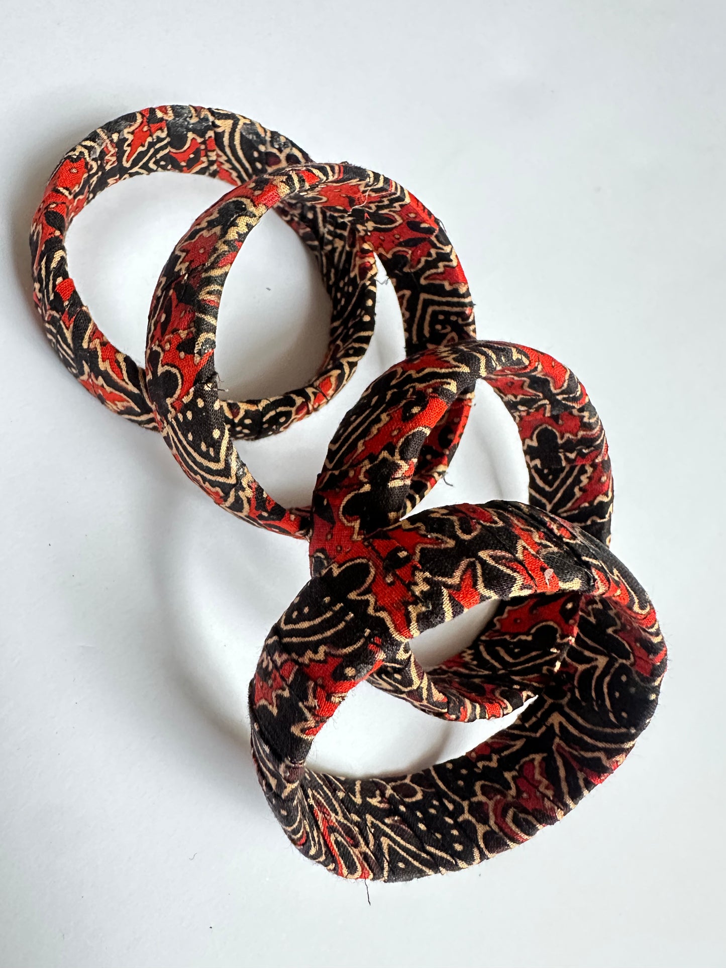 Patterned handmade fabric bangle in red, black, and beige on a white background