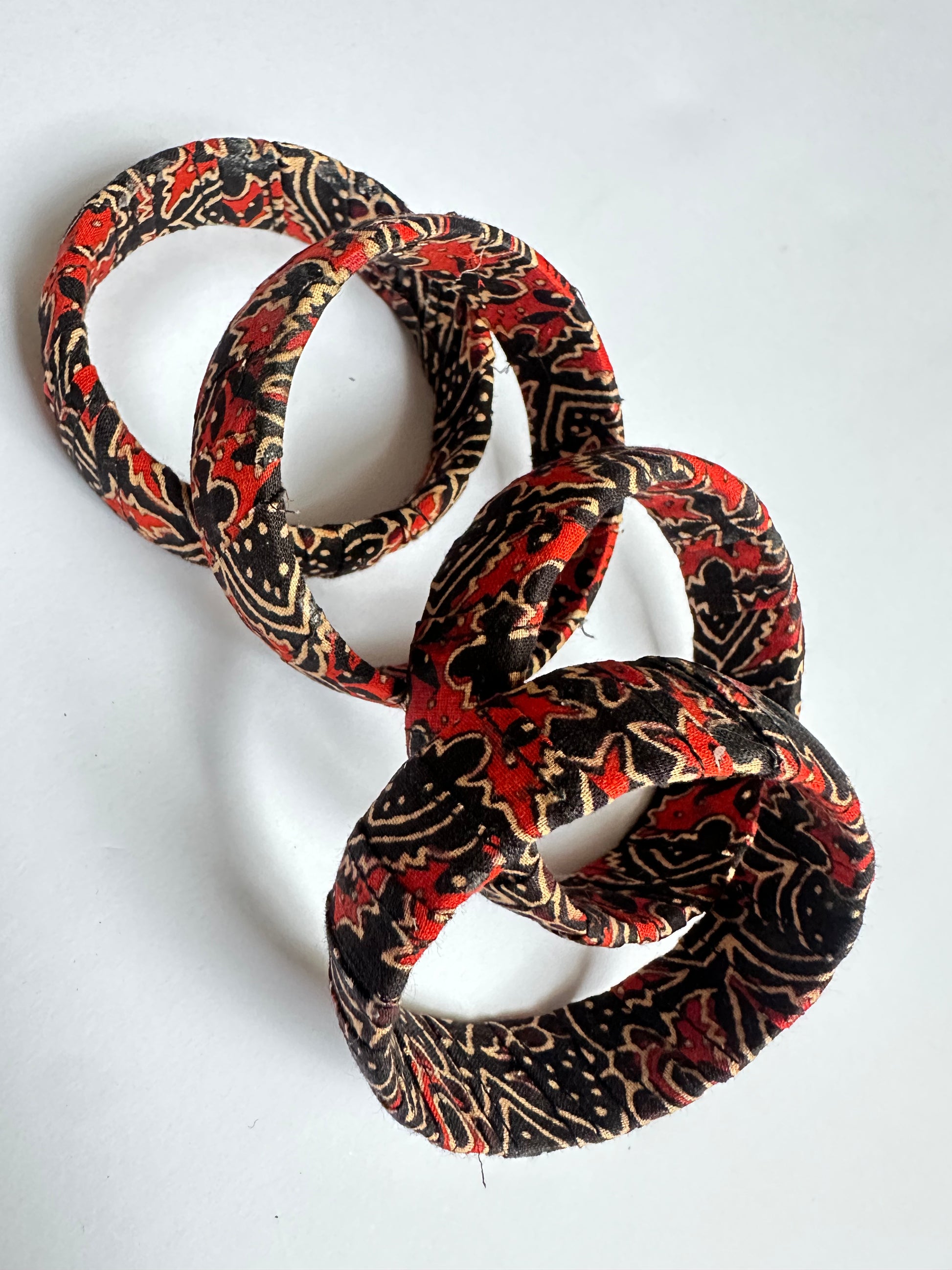 Patterned handmade fabric bangle in red, black, and beige on a white background
