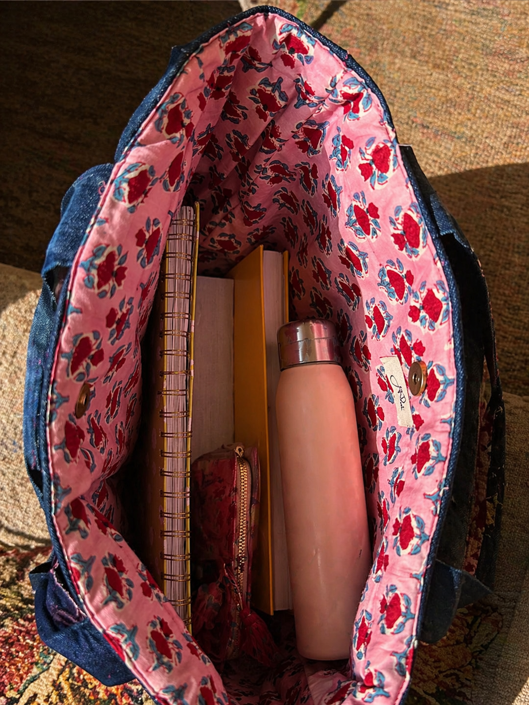 Denim bag with floral-patterned bag interior with a bottle and other items on a textured surface