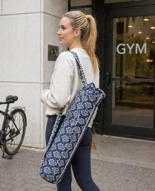 A woman carrying a blue and white patterned yoga mat bag with a gym entrance in the background
