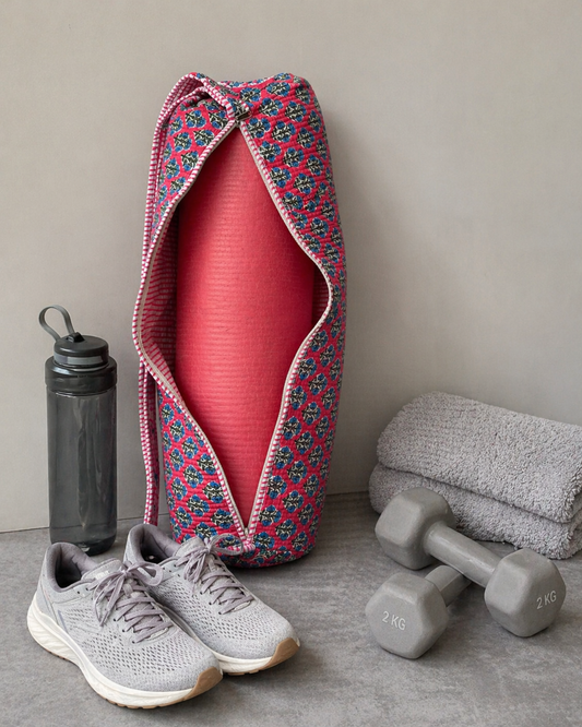 A pink floral yoga mat cover with a yoga mat in it. Lying on the side are sneakers, a water bottle, and dumbbells on a grey surface.