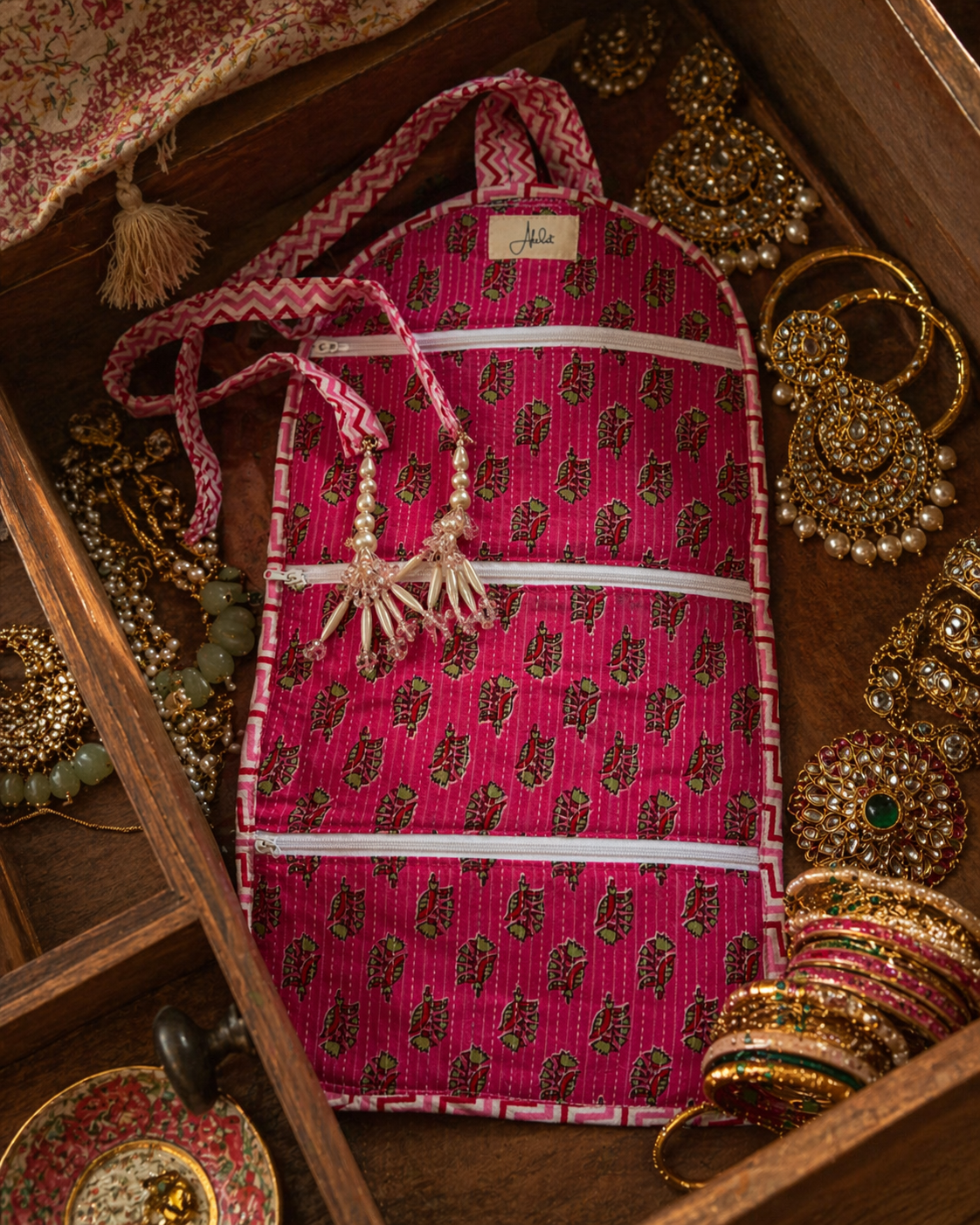 Pink block-print patterned interior of a organiser bag with jewellery on a wooden surface