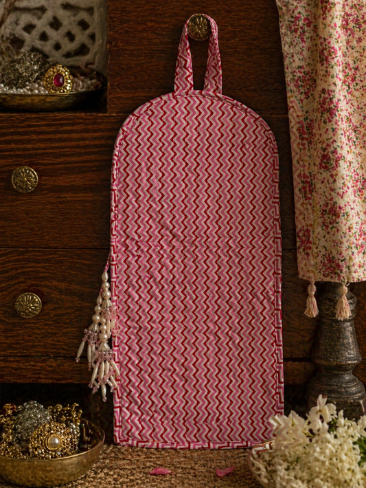 A red and white zigzag patterned bag with tassels, hung with a loop on a wooden surface.