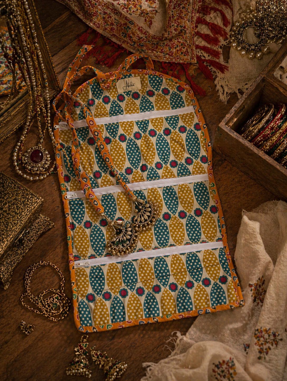 Decorative interior of a jewellery organiser in pattern similar to pineapple pattern surrounded by jewellery on a wooden surface