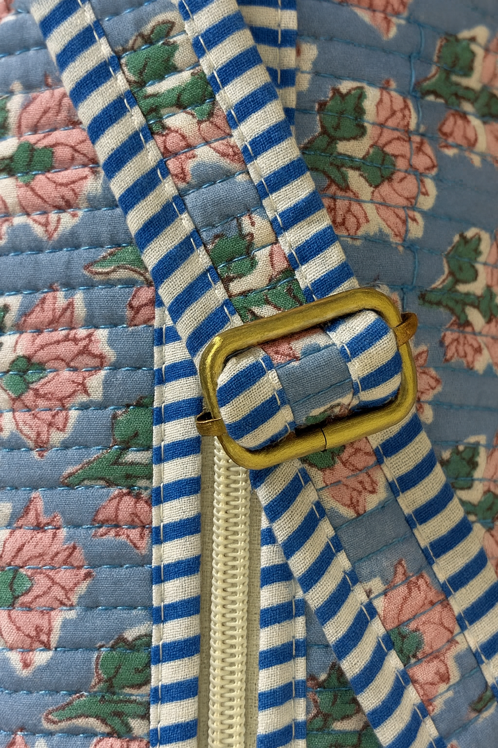 Close-up of a blue and white striped belt with a gold buckle on a floral fabric background.