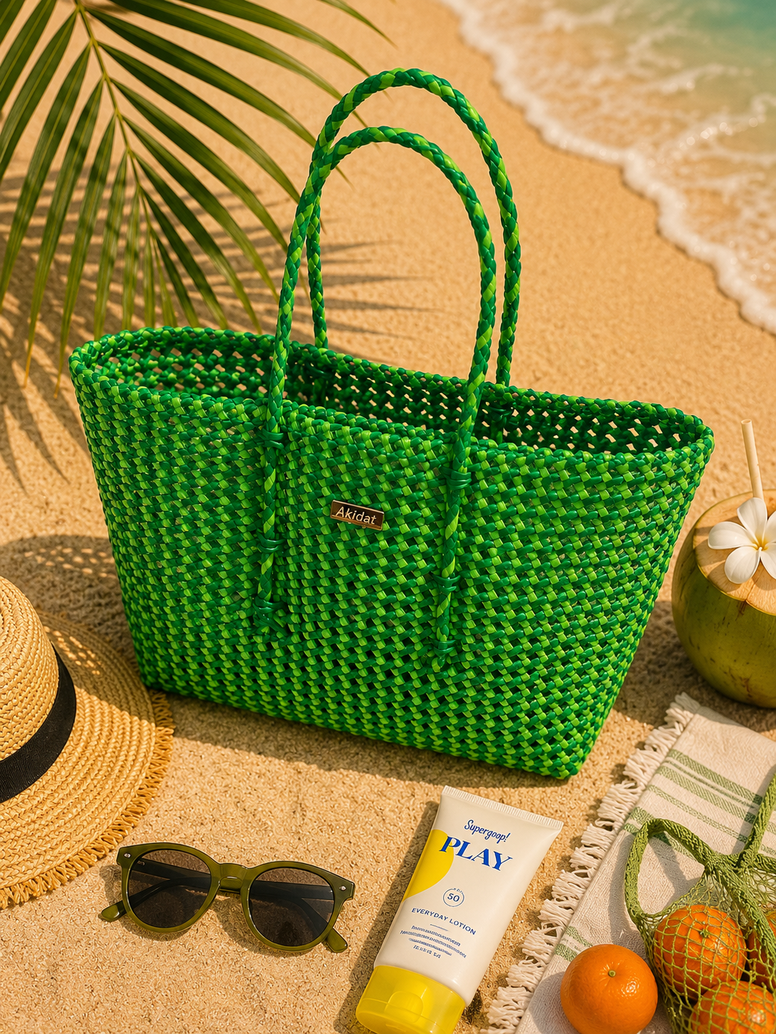 A green and fluorescent green recycled plastic woven tote bag on a beach with sunglasses, sunscreen, and fruit.