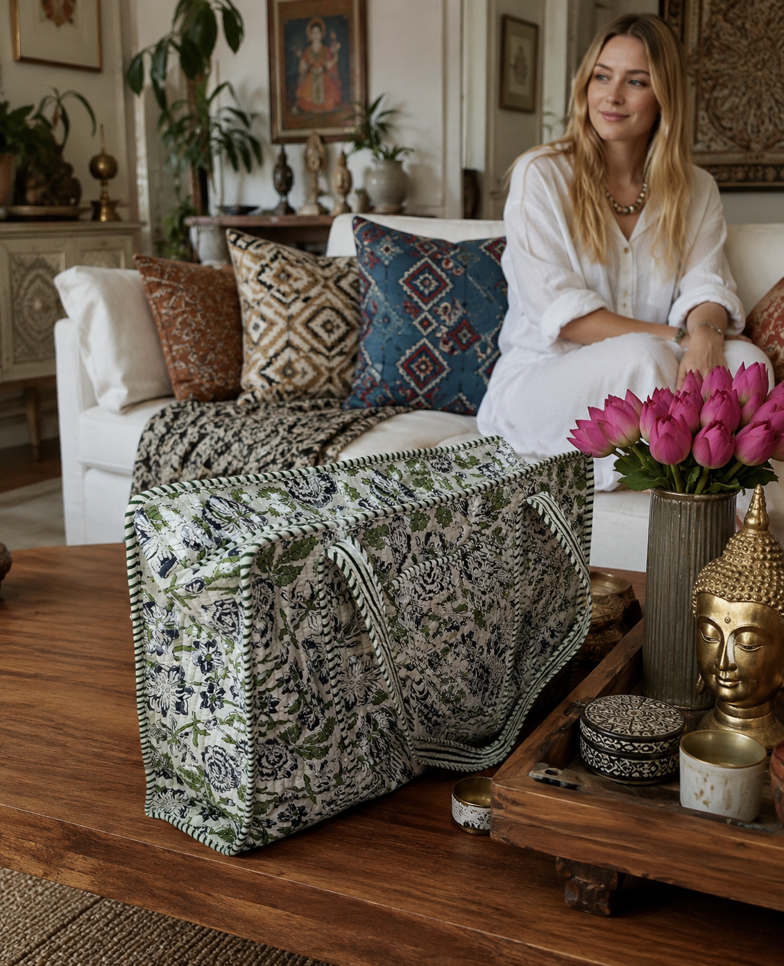 Woman sitting on a couch with patterned cushions and a floral arrangement in a cosy living room. A quilted floral tote bag kept on the wooden table in front of her