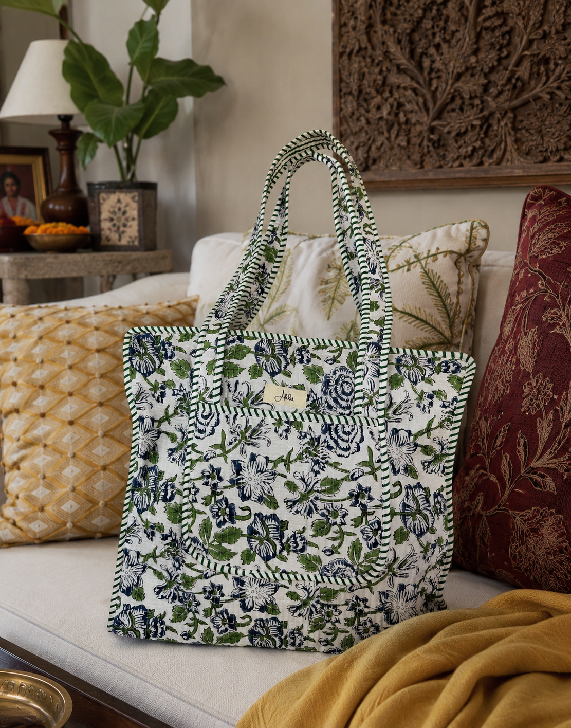 A floral-patterned quilted tote bag on a couch with decorative pillows and a plant in the background
