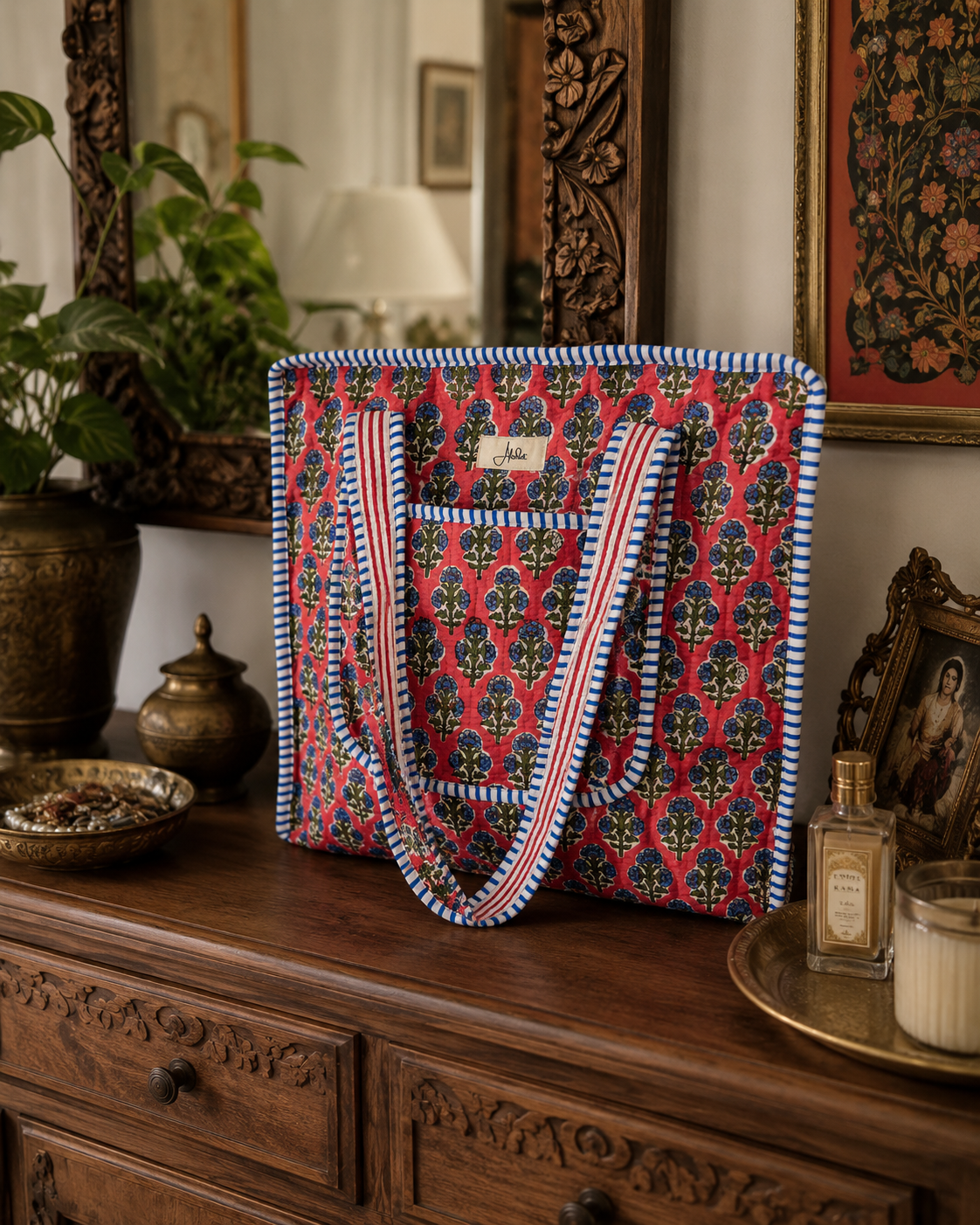 A floral-patterned quilted bag with pockets on a wooden dresser with decorative items