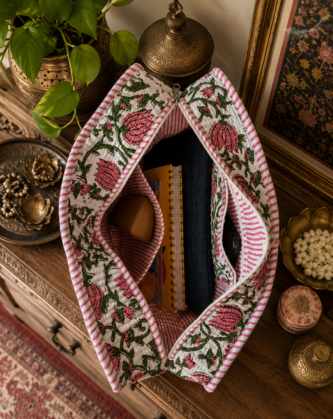 Decorative floral quilted tote bag with an open zipper and laptop sleeve, notepads, a sunglass cover and a mobile phone inside on a wooden surface with decorative items.