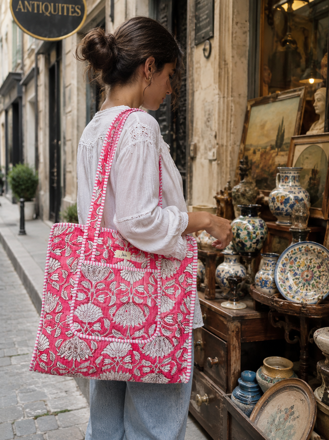 A woman is shopping in an antique store with a pink and white floral-patterned quilted tote bag.