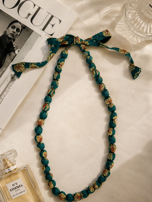 Teal coloured fabric beaded necklace with floral patterns on a magazine and Chanel perfume bottle