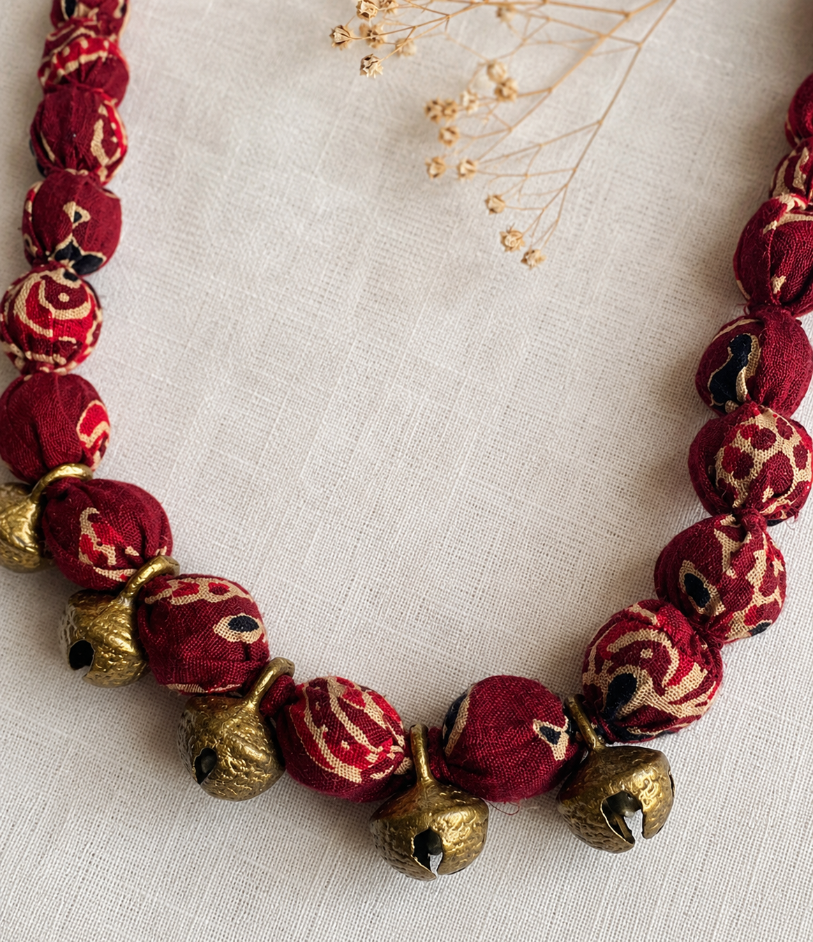 Fabric Necklace with red beads and gold bells on a light fabric background