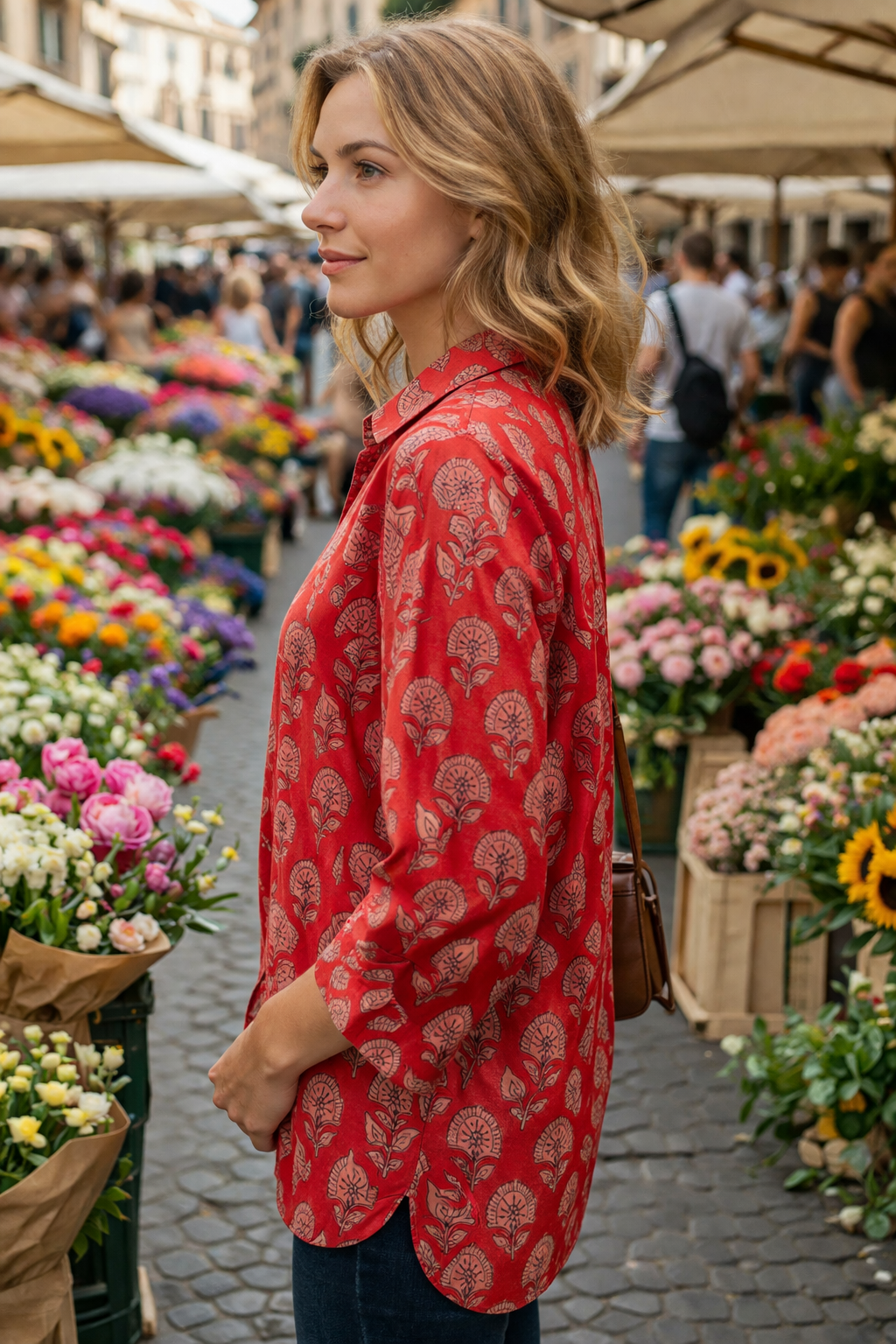 A woman in a red patterned cotton blockprint shirt standing in a market with flowers around her.