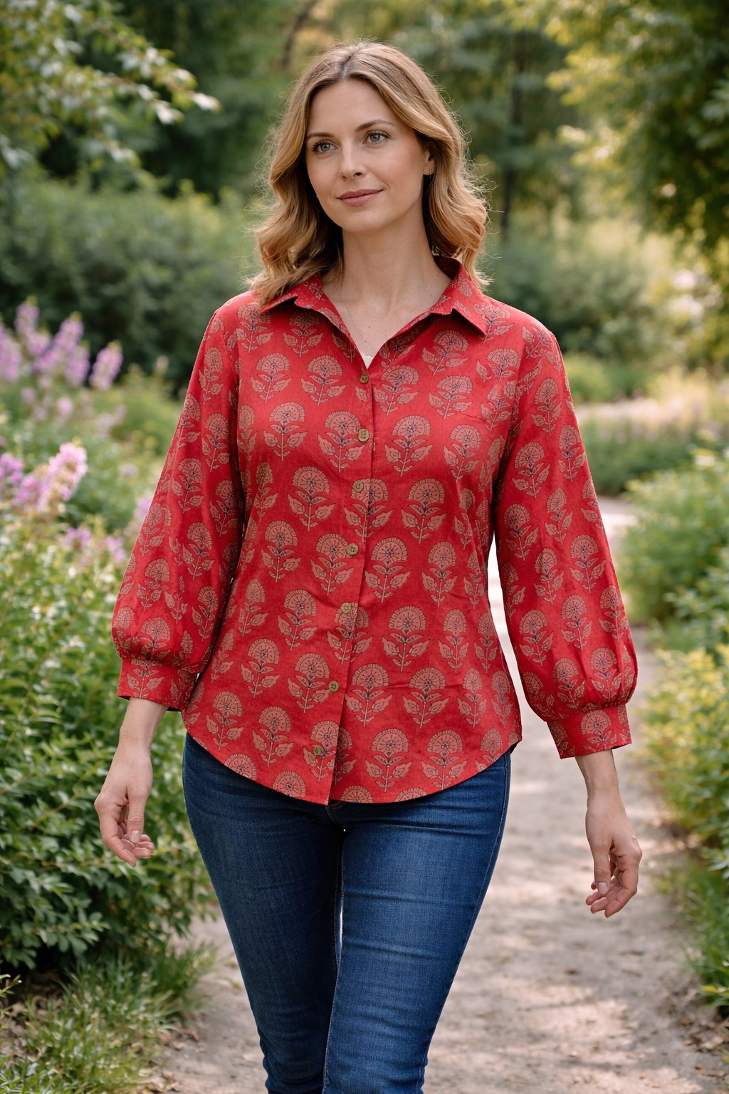 A woman wearing a red floral cotton block-print shirt and blue jeans walking through a garden.