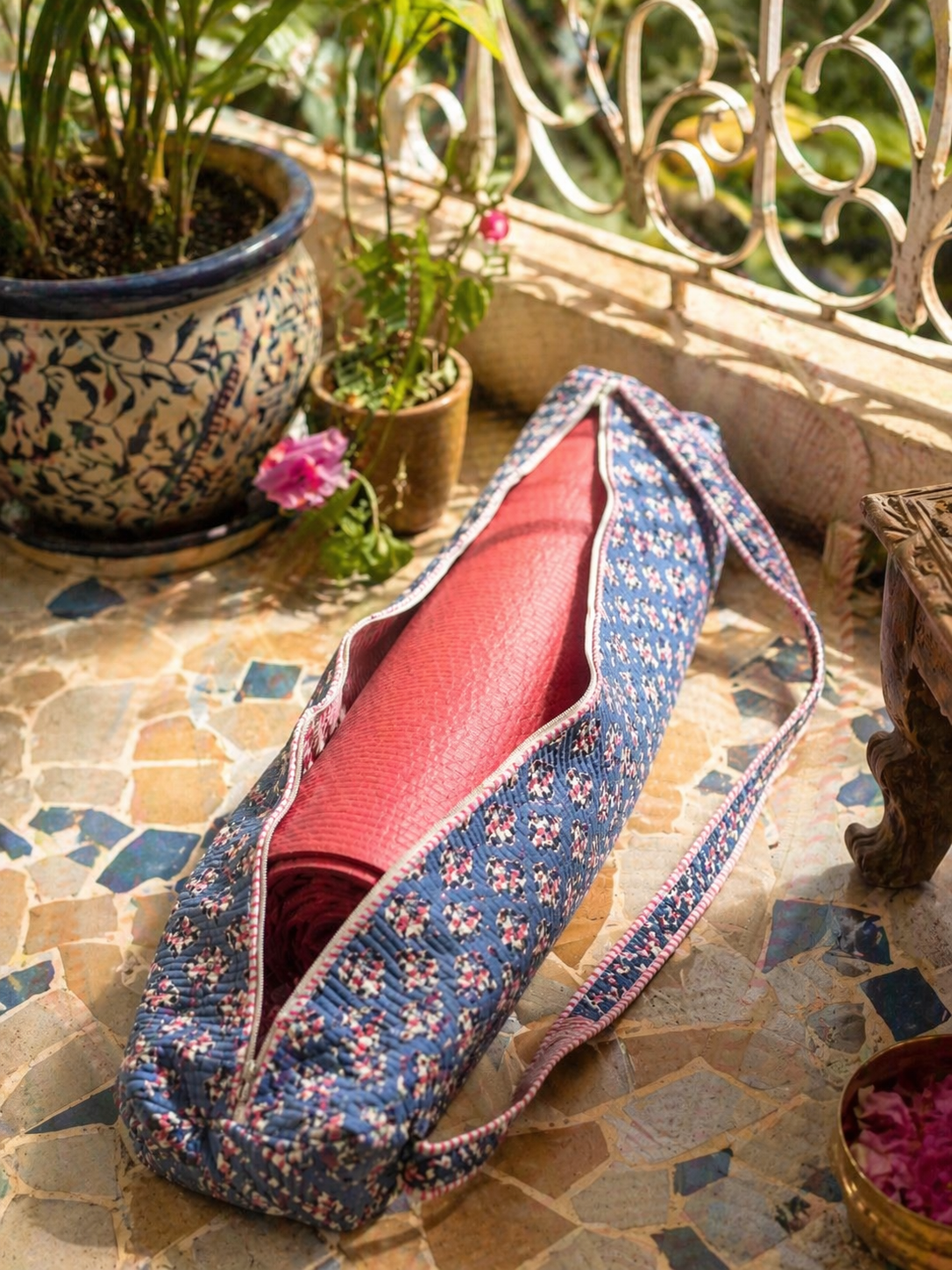 Pink Yoga mat in a blue floral-patterned cover on a stone surface with plants in the background