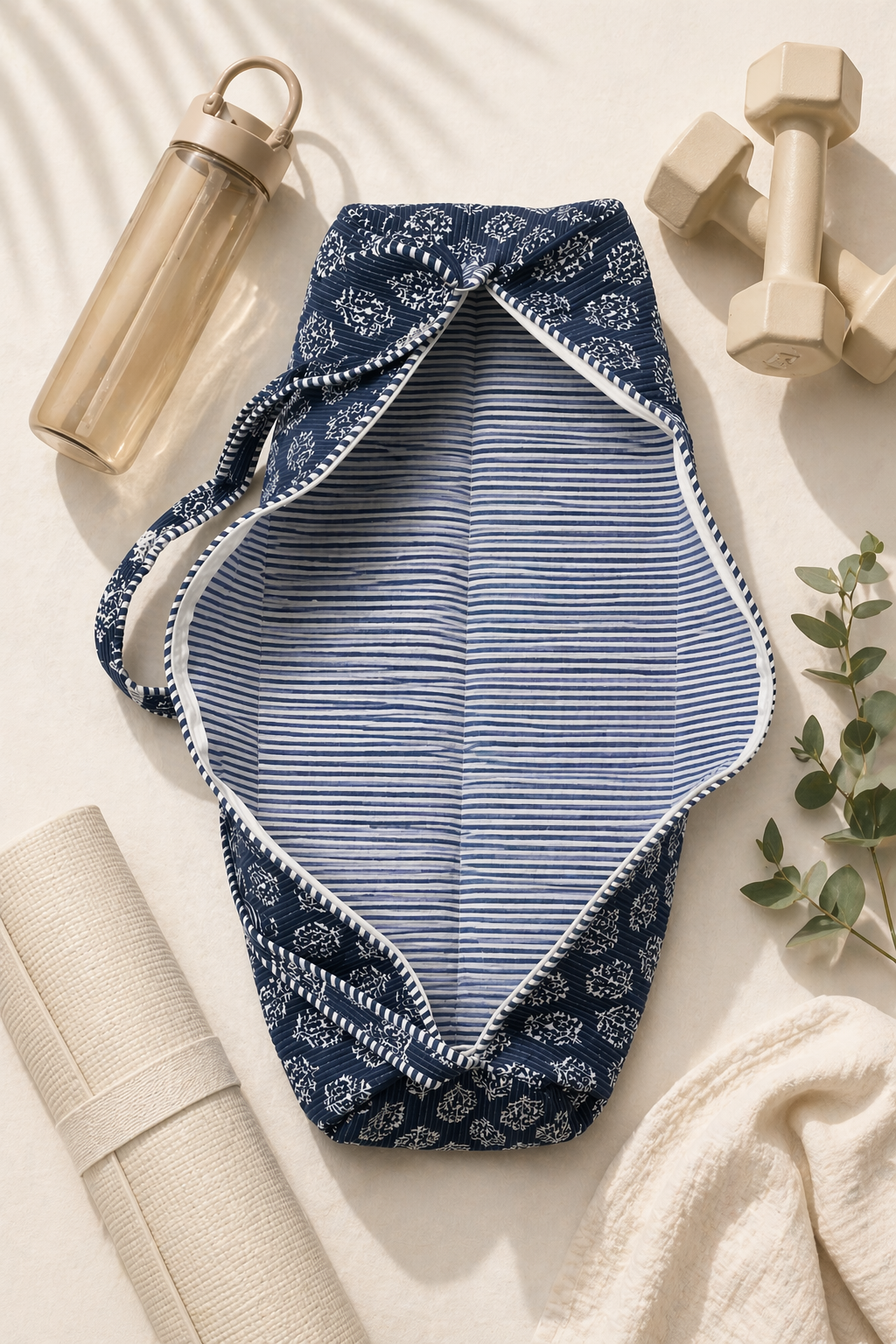 A blue and white patterned yoga mat cover with a zip opening and stripped interior showing on a neutral background with a yoga mat, water bottle, and dumbbells.