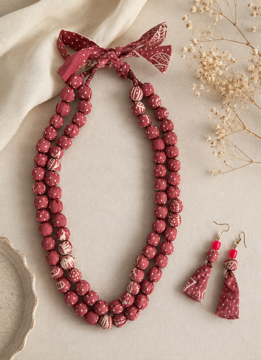 A crimson-pink fabric beaded necklace with matching earrings on a neutral background