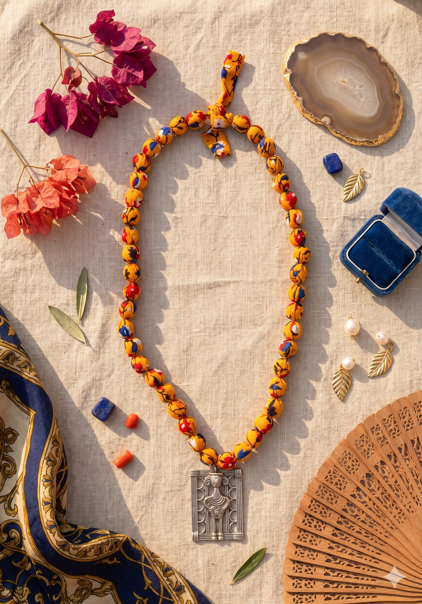 A colourful deep yellow beaded necklace with a Mettalic pendant on a textured surface with decorative items.