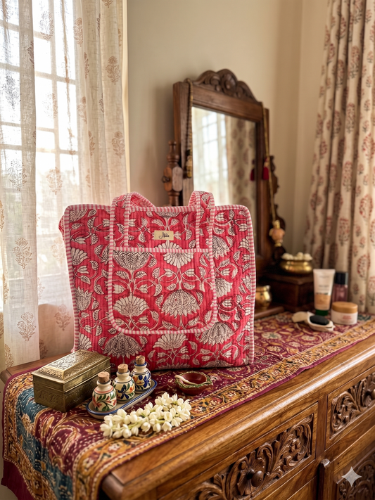 Crimson-coloured quilted floral tote bag with block print placed on a wooden dresser. 