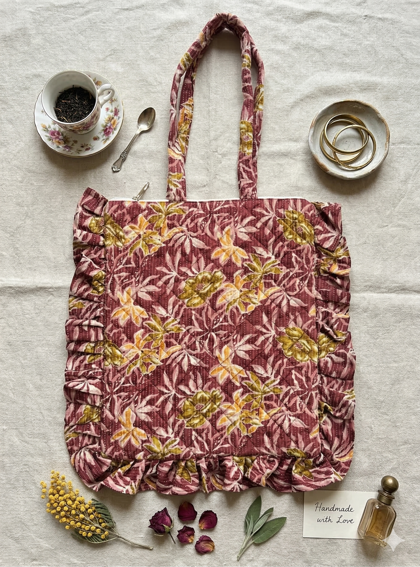 A floral-patterned quilted zippered frill tote bag on a textured surface with a cup of tea and saucer.