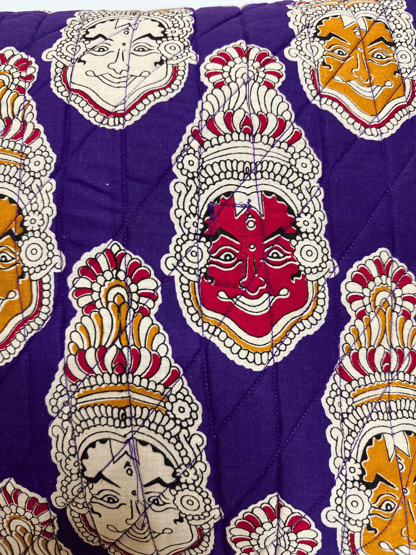 Decorative quilted cushion fabric with colourful face mask patterns on a purple background