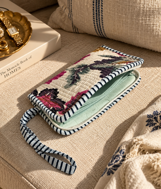 A floral-patterned quilted wallet clutch on a beige sofa with open zipper showing inner water-resistant interior